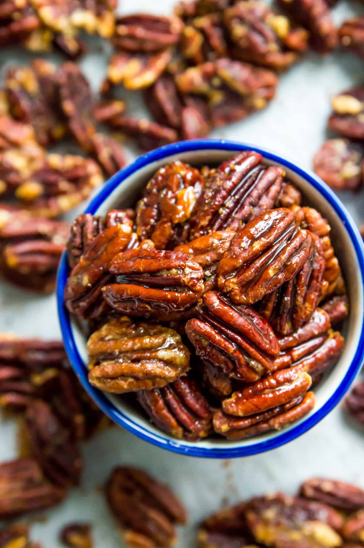 A bowl of roasted honey dijon pecans surrounded by other glazed pecans.