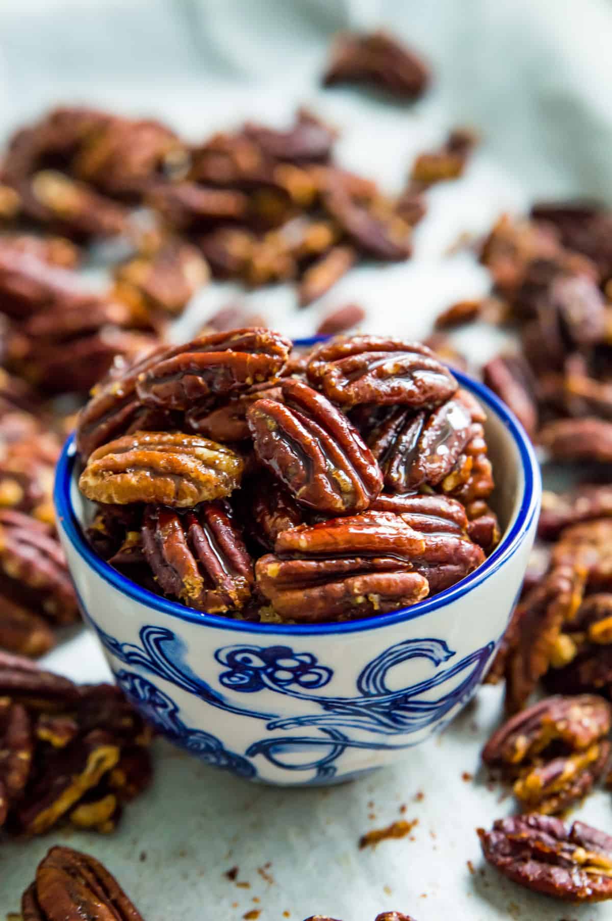 A bowl of honey dijon pecans with glazed pecans surrounding it.