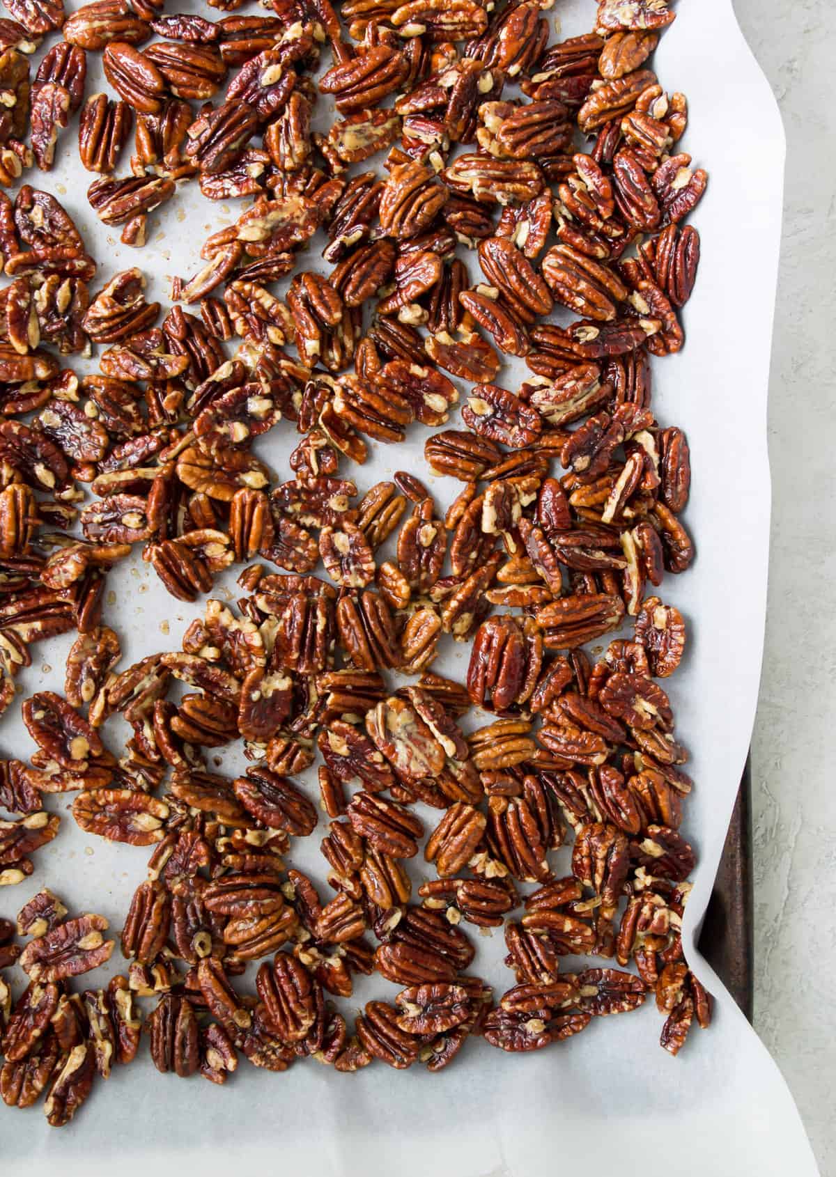 Glazed pecans on a piece of parchment paper on a baking sheet.
