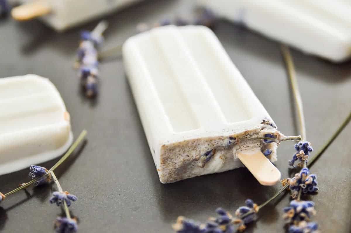 Lavender vanilla popsicles on a tray with lavender flowers around them. 