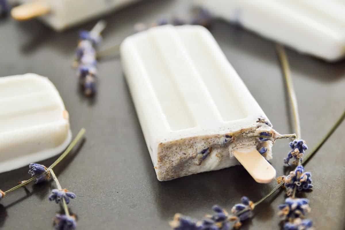 Lavender vanilla popsicles on a tray with lavender flowers around them.