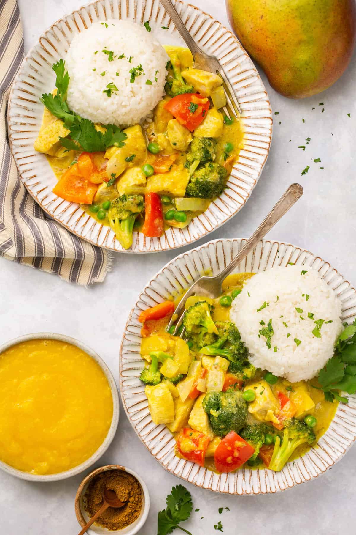 Bowls of mango chicken curry topped with white rice and garnished with cilantro.