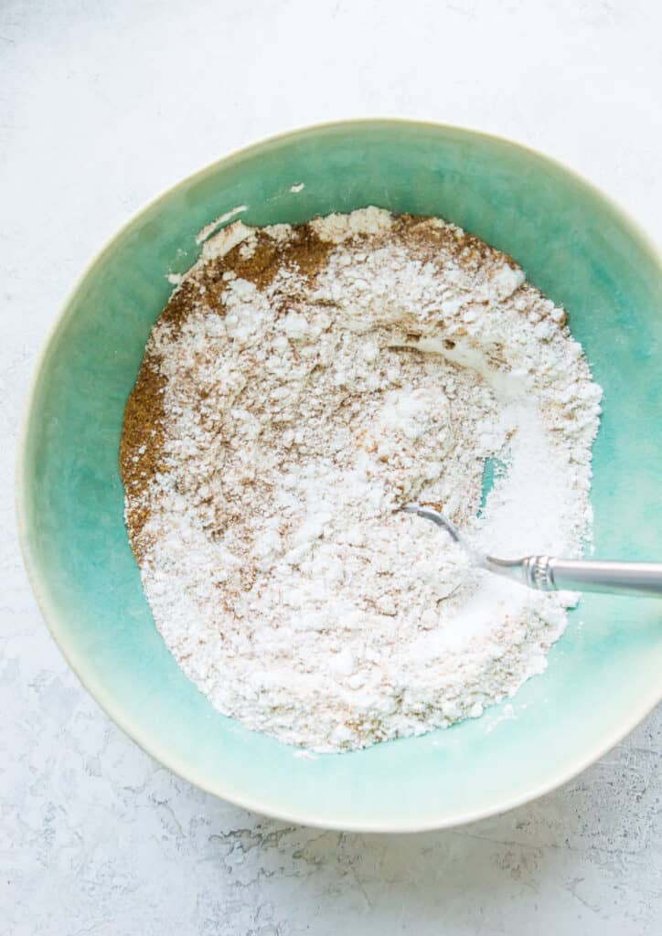 A bowl filled with flour, coconut sugar, cinnamon and baking soda with a spoon in it.