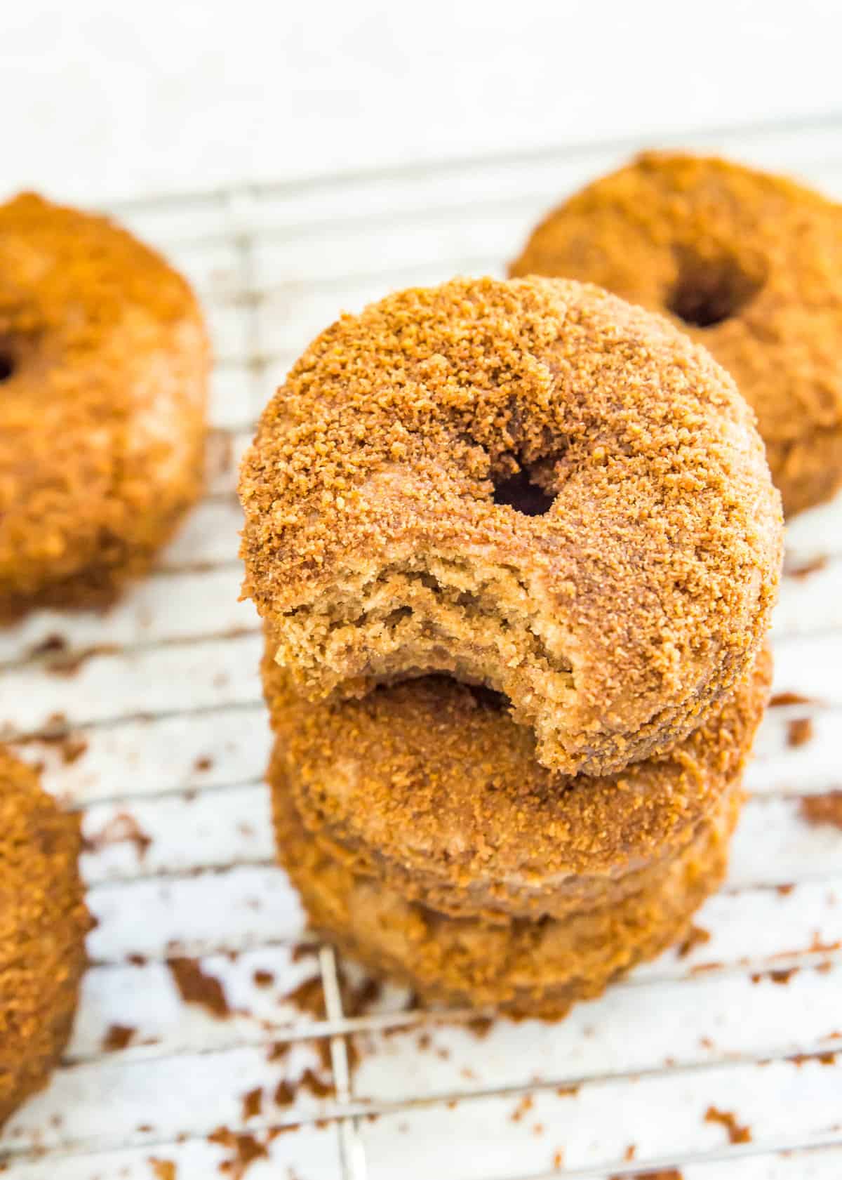 A stack of three vegan donuts coated in cinnamon and sugar and the top donut has a bite out of it.