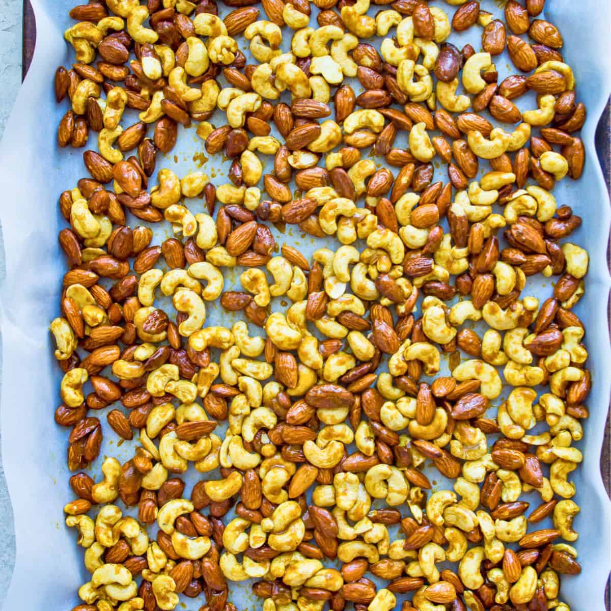 A baking sheet lined with parchment paper with cashews and almonds spread over it.