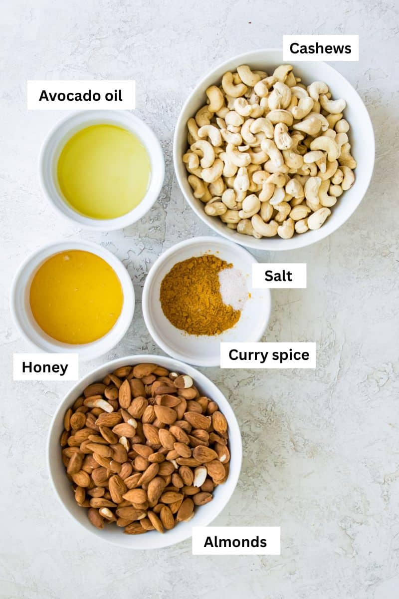 Different foods separated into bowls including cashews, almonds, honey, oil and curry spice.