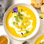 A bowl of paleo curried butternut squash soup garnished with flowers and fresh parsley.