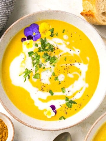 A bowl of paleo curried butternut squash soup garnished with flowers and fresh parsley.