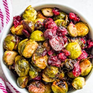A bowl of roasted Brussels sprouts with cranberries surrounded by a tea towel.