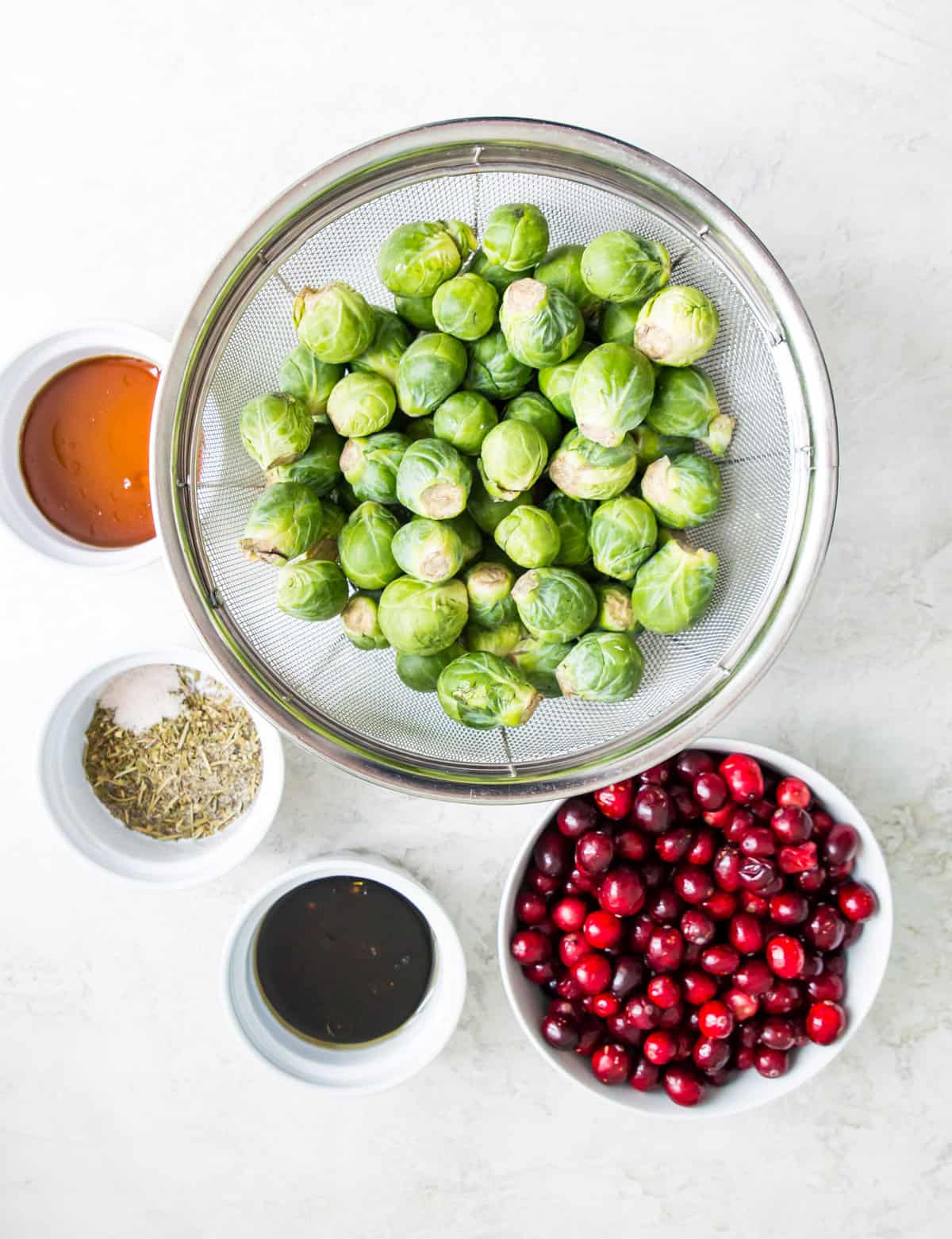 The ingredients needed for making roasted Brussels sprouts with cranberries separated into small bowls.