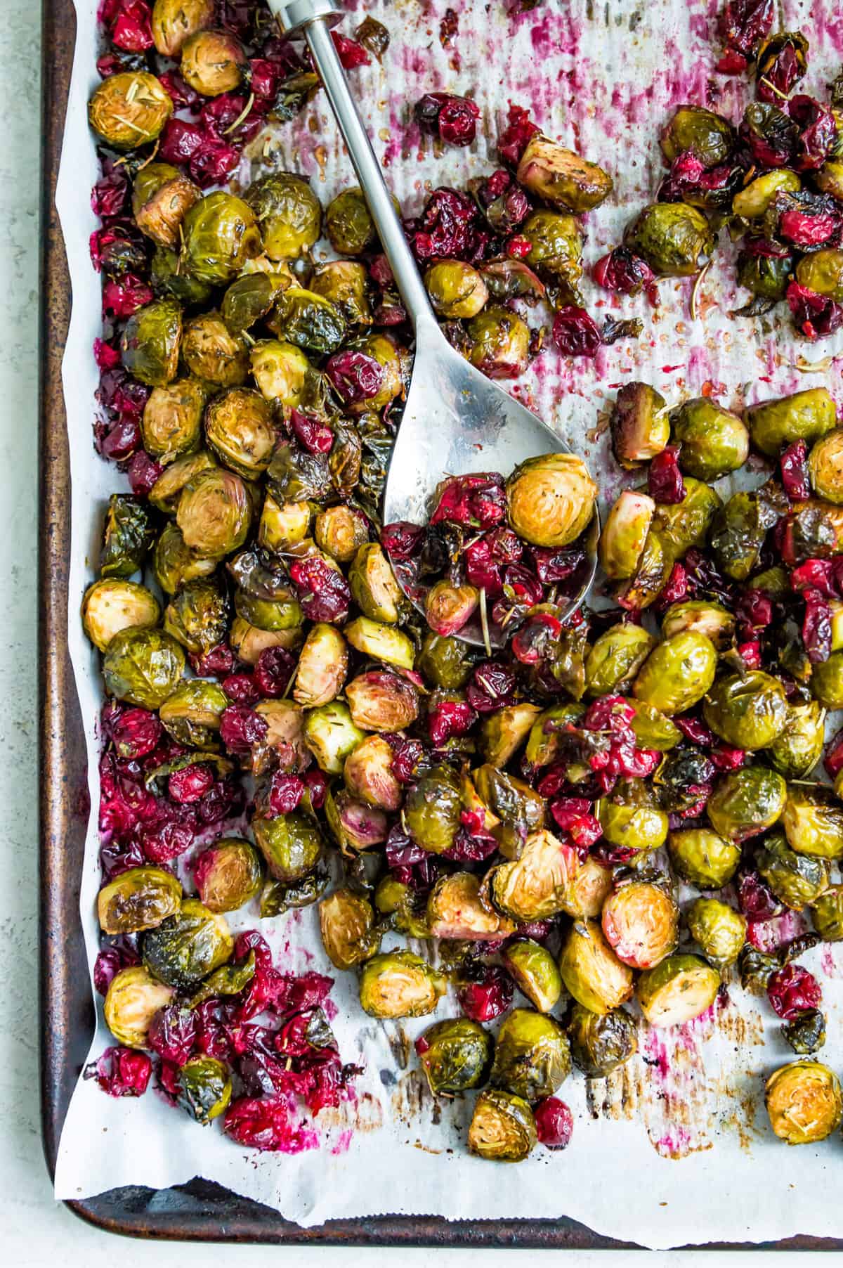 A pan of roasted Brussels sprouts with cranberries and a serving spoon. 
