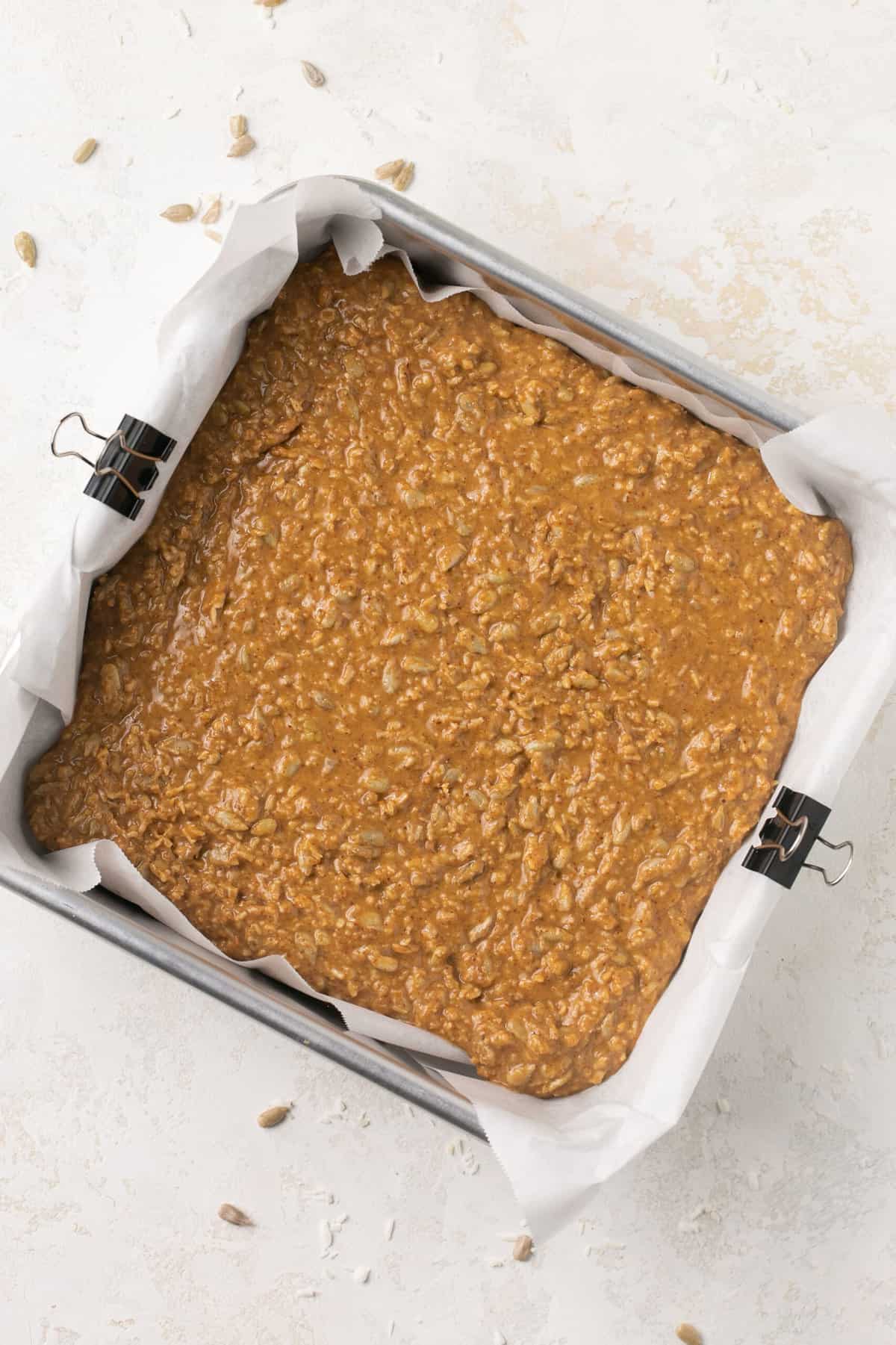 A square baking pan lined with parchment paper with almond butter bars in it.