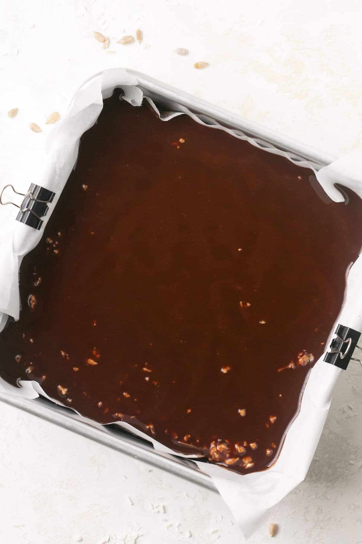 A square baking pan lined with parchment paper with melted chocolate in it.