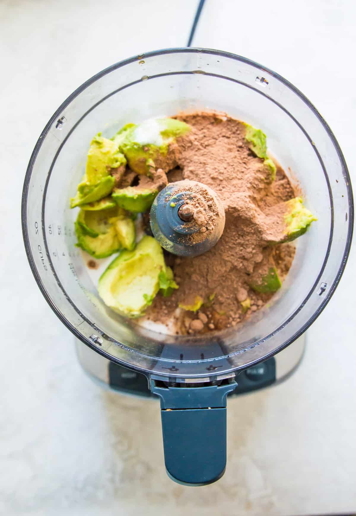 A food processor filled with avocado flesh, cocoa powder and maple syrup.