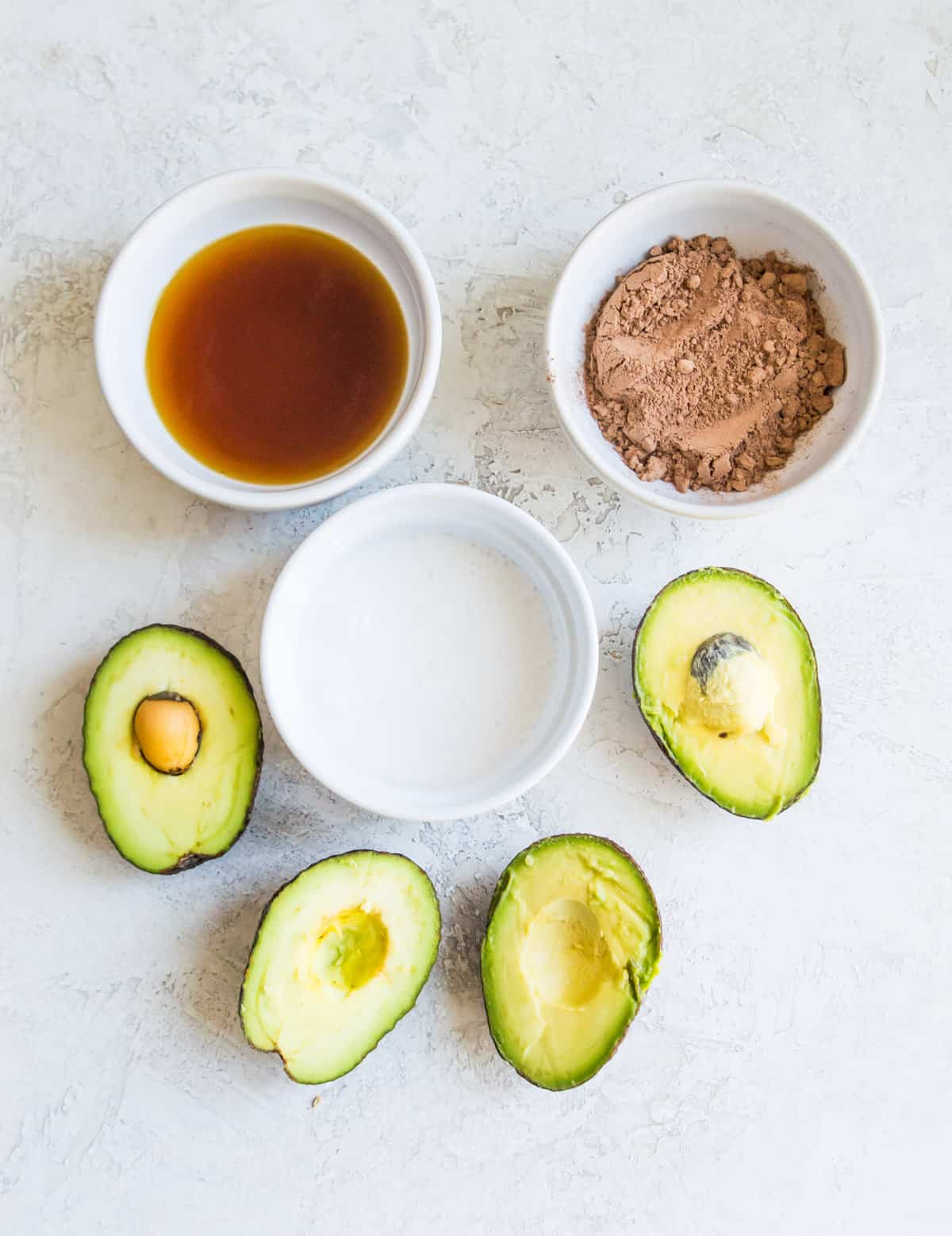 The ingredients needed to make chocolate avocado mousse separated into small bowls. 