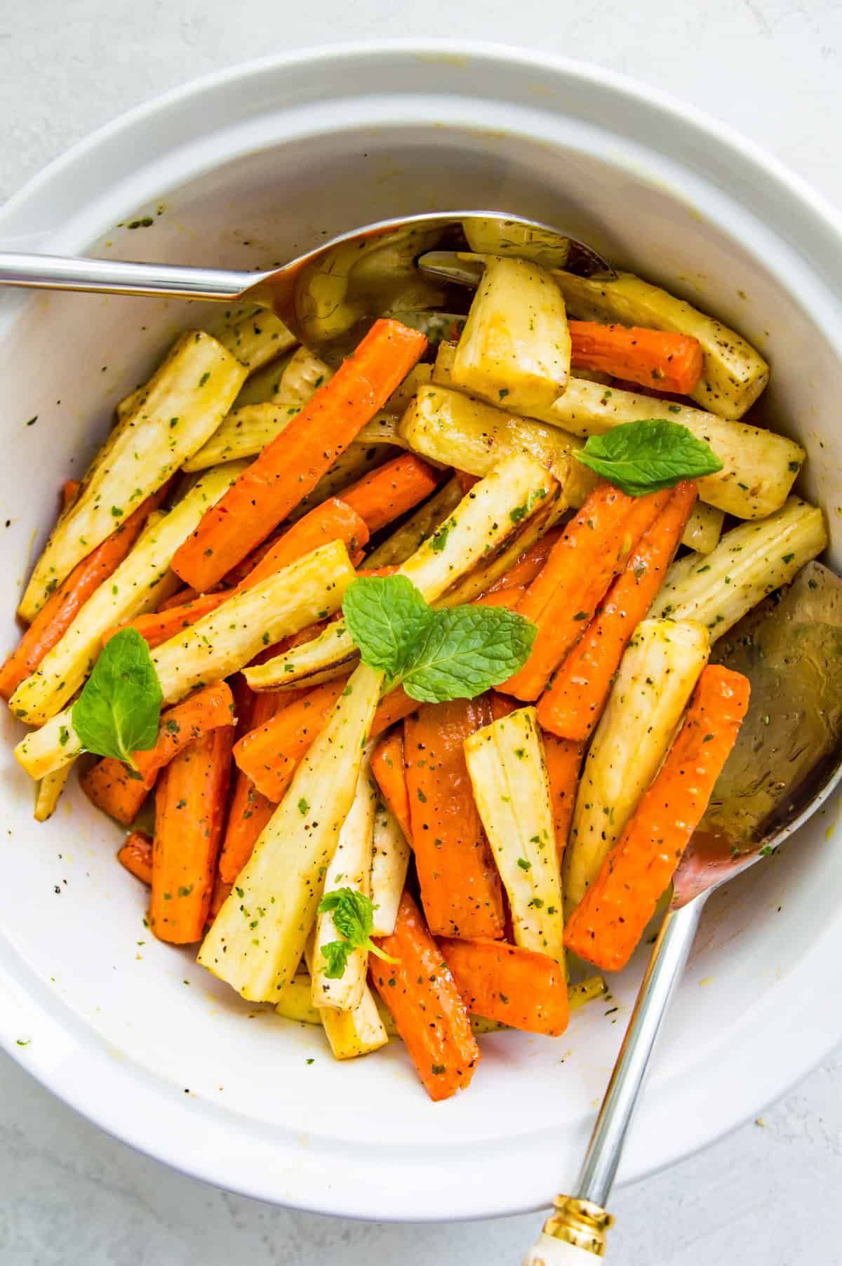A bowl of roasted carrots and parsnips with a serving spoon in it.