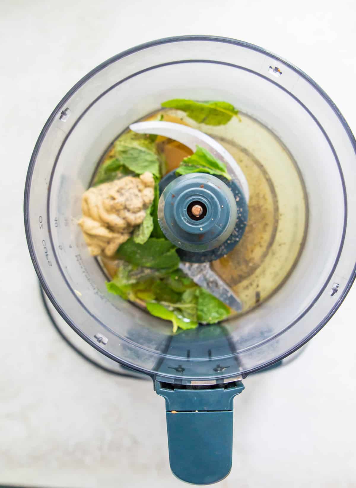 A food processor filled with the ingredients needed to make a mint maple vinaigrette.
