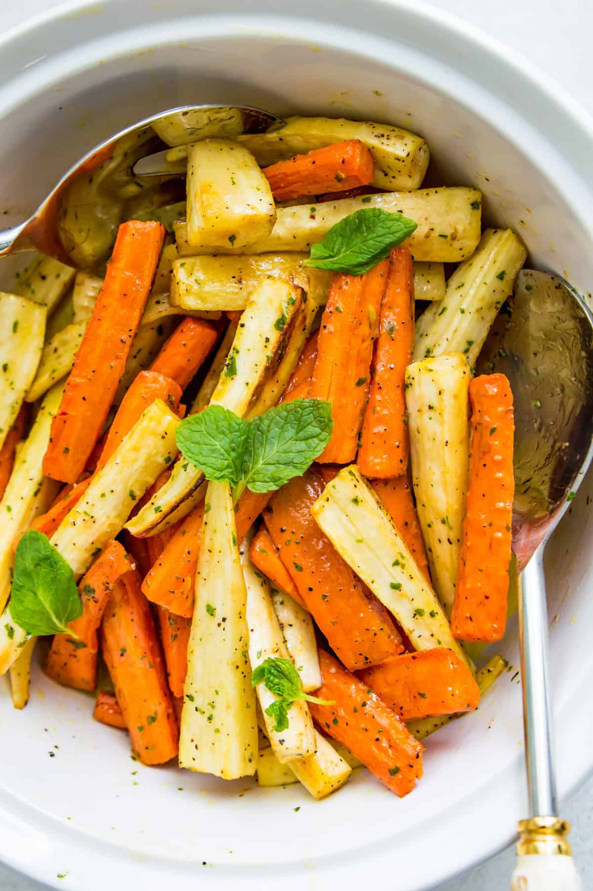 A bowl of roasted carrots and parsnips with mint leaves on top.