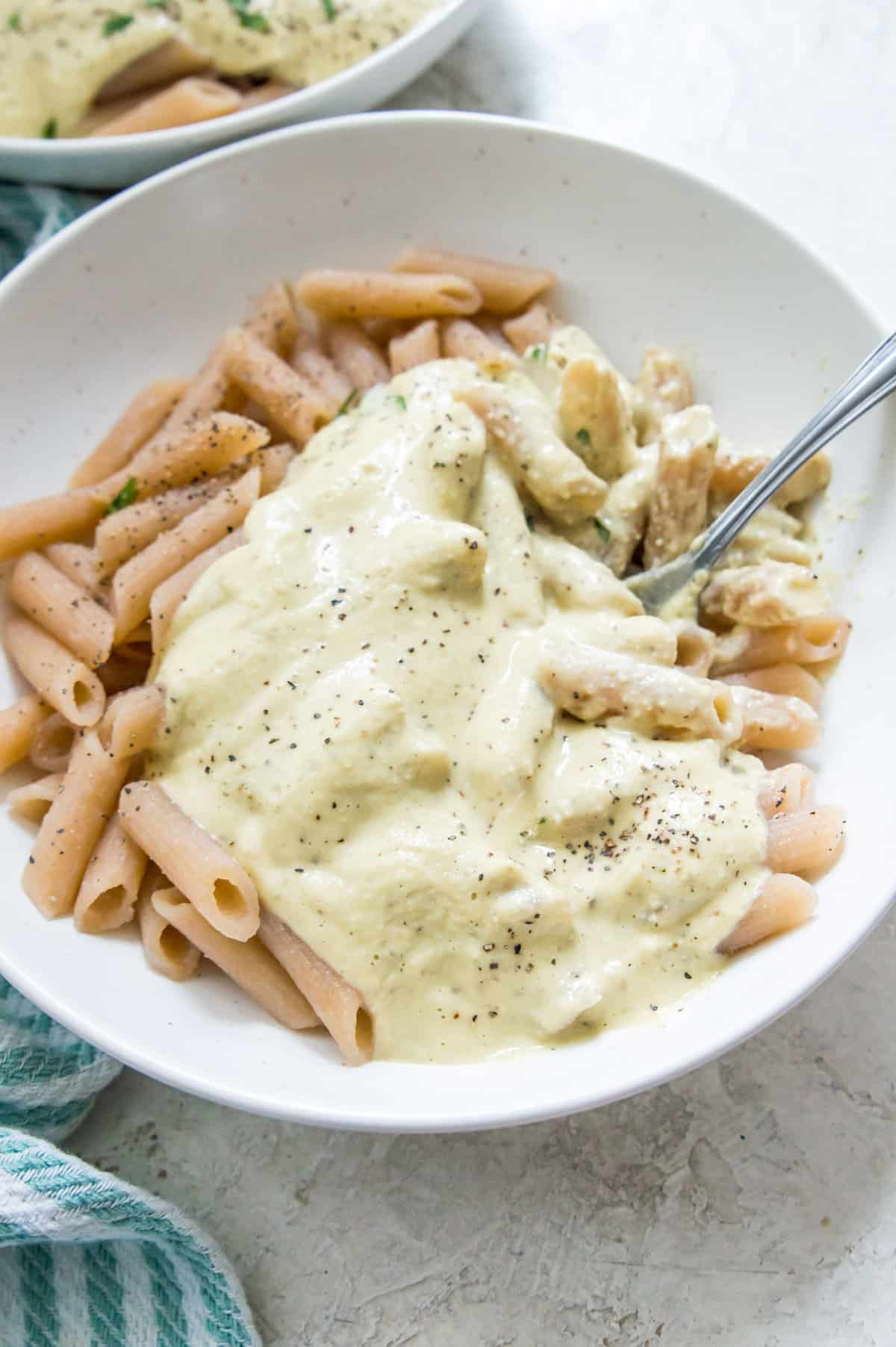 A bowl of pasta with Alfredo sauce on it and a spoon in it.