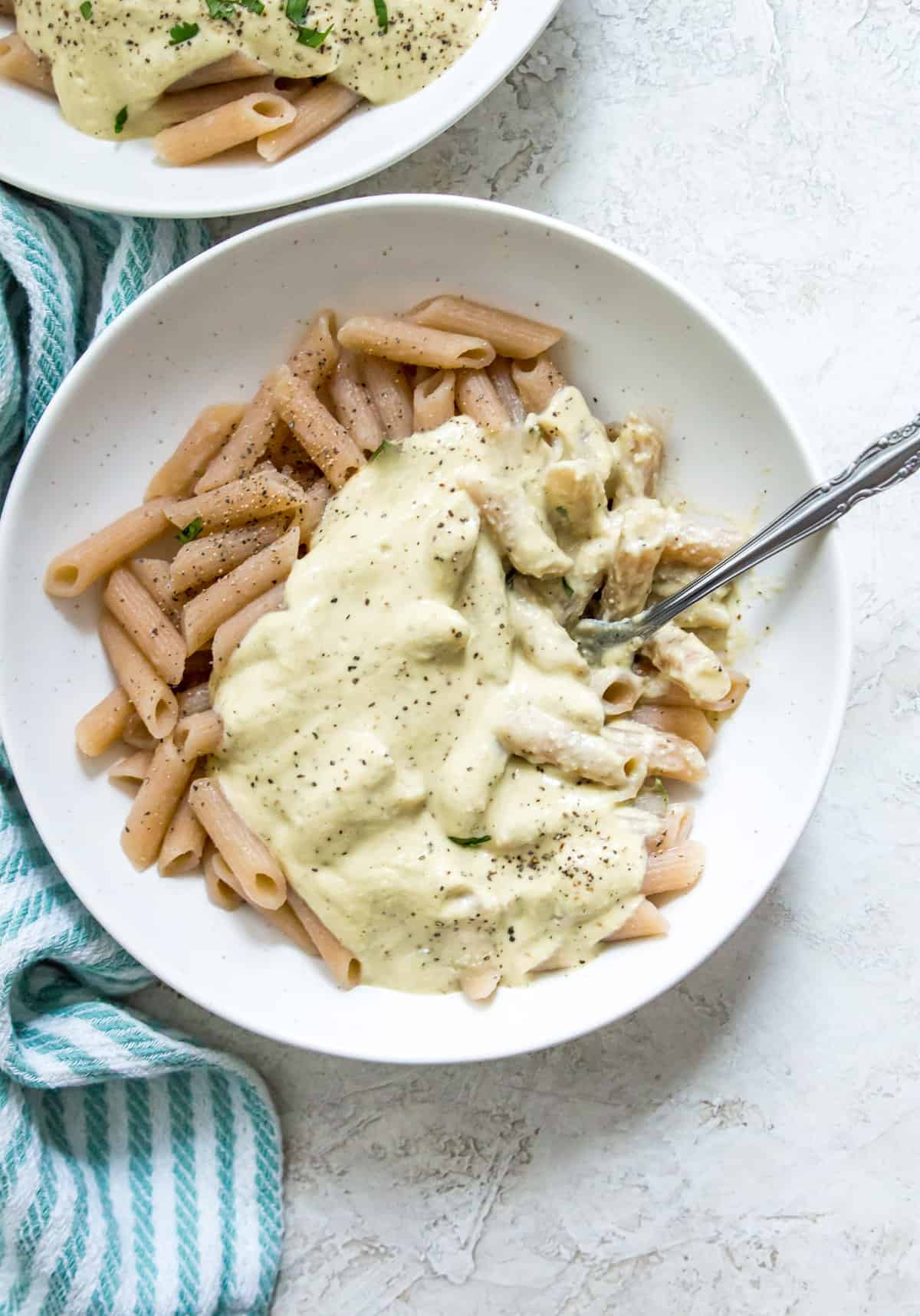 A bowl of pasta topped with a creamy Alfredo sauce and a spoon in it.