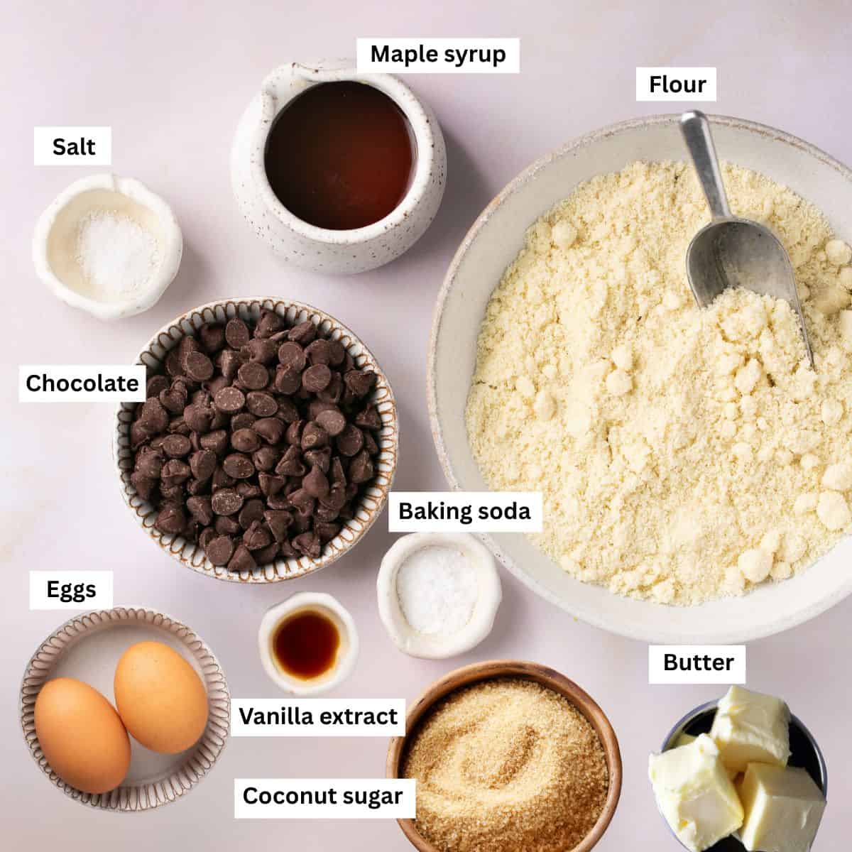 The ingredients needed for making cookies separated into bowls including flour, eggs, chocolate chips, butter, coconut sugar and baking soda.