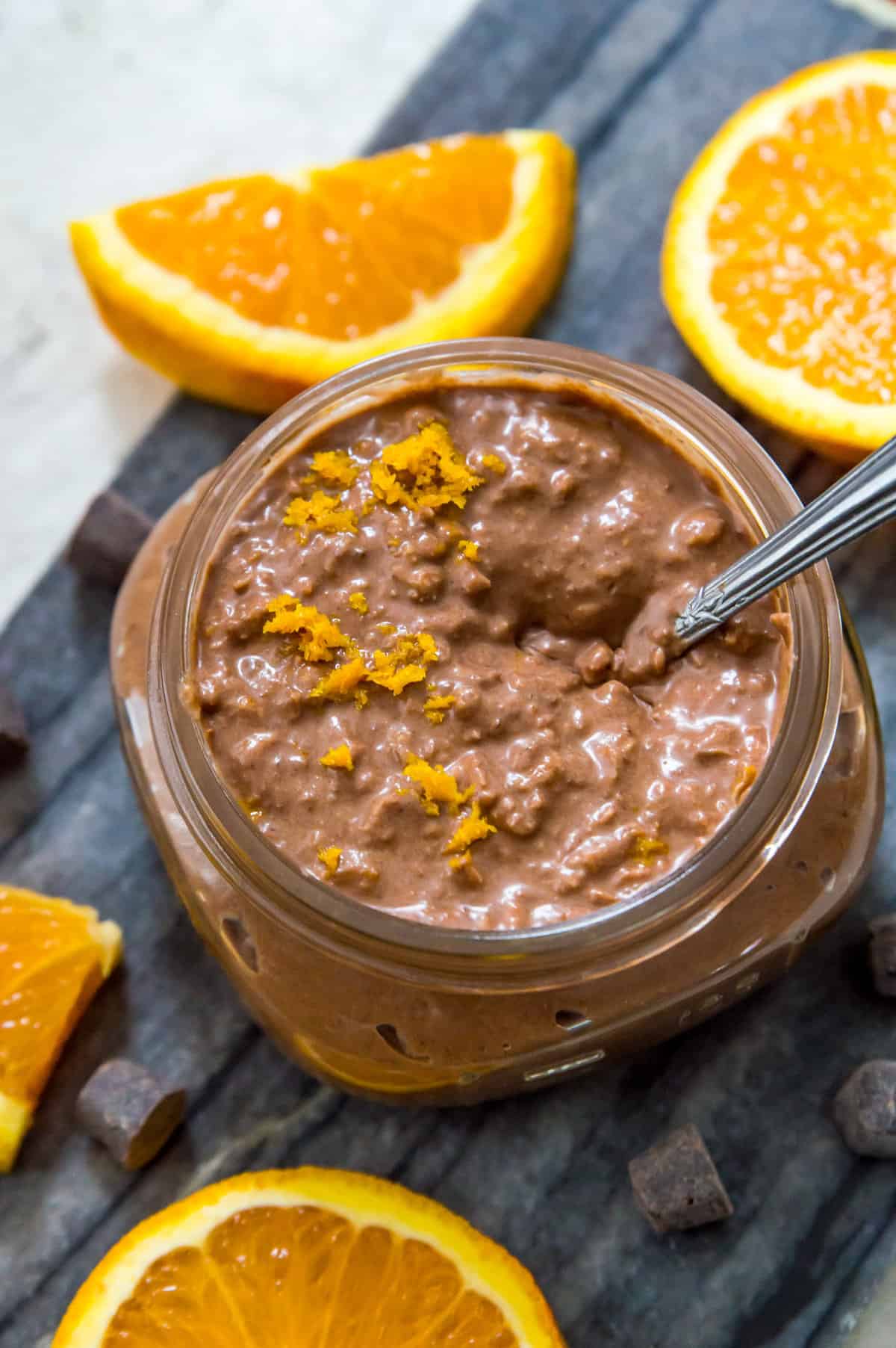 A jar of orange chocolate overnight oats with a spoon in it and garnished with orange zest.