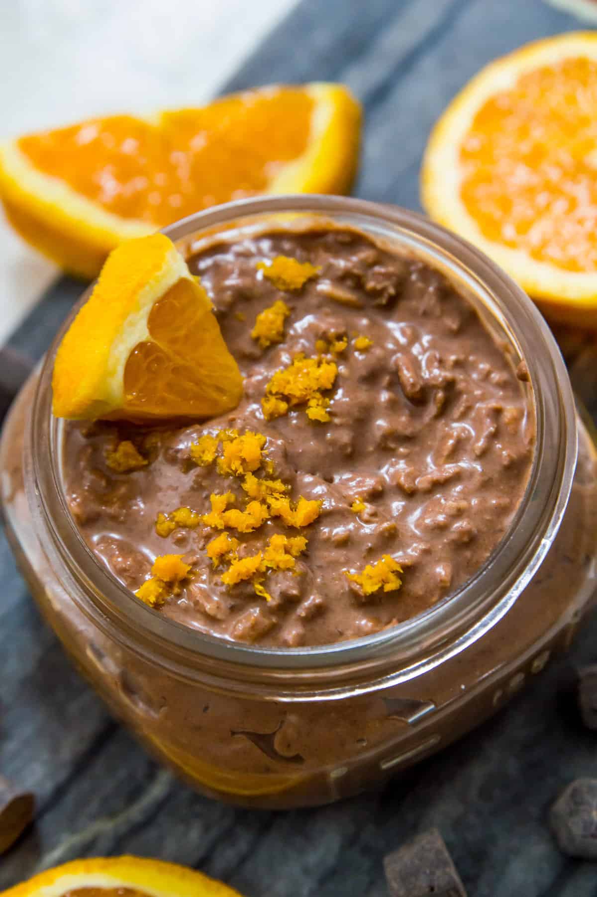 A jar of chocolate orange overnight oats garnished with orange zest and an orange wedge in it.