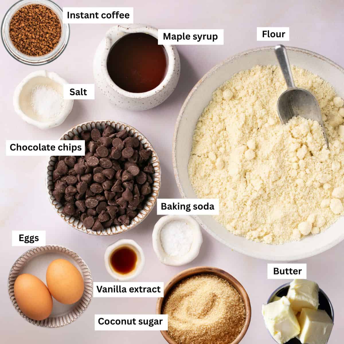 The ingredients needed for making cookies separated into bowls including flour, eggs, chocolate chips, butter, coconut sugar and baking soda.