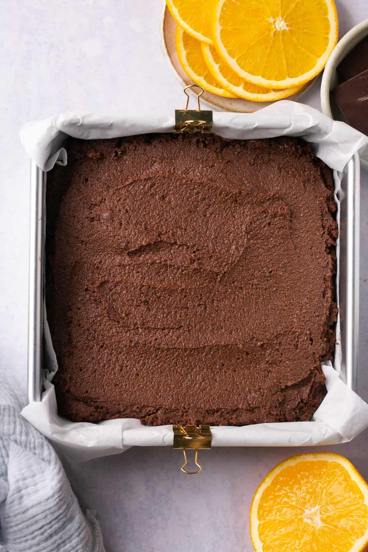 Brownie batter in a baking dish lined with parchment paper and surrounded by orange slices. 