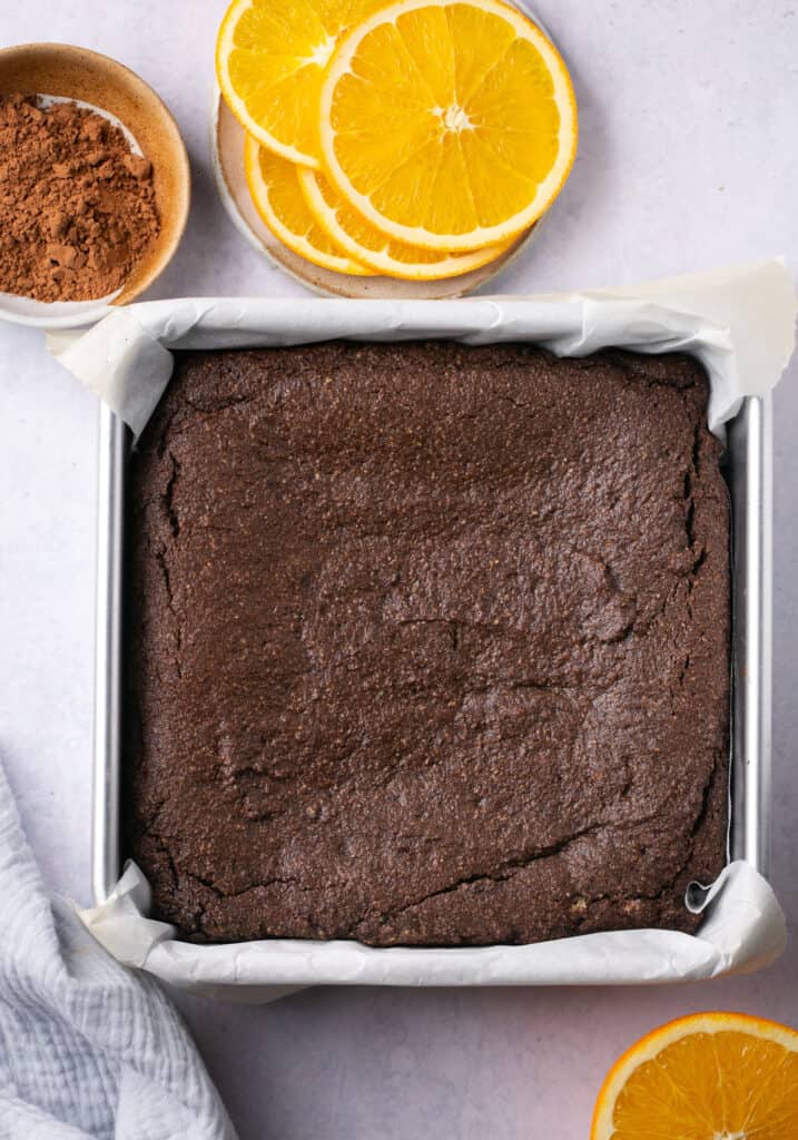 A square baking pan lined with parchment paper with brownie batter spread out in it.