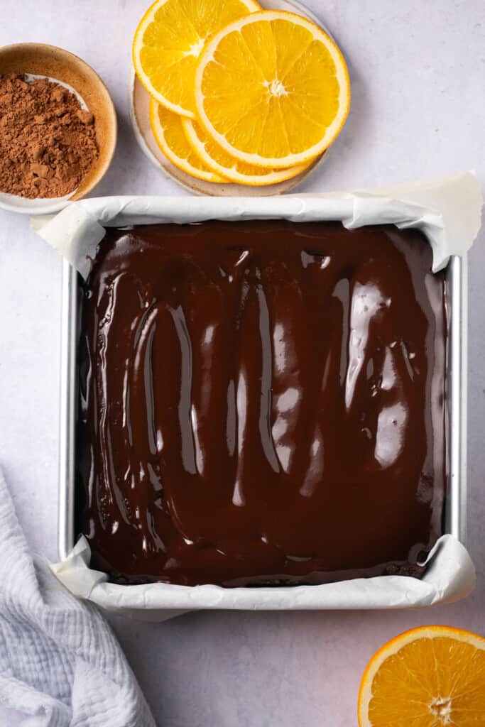 A square baking pan with a batch of brownies in it with chocolate icing on top.