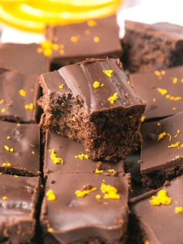 A stack of orange chocolate brownies, one with a bite out of it.