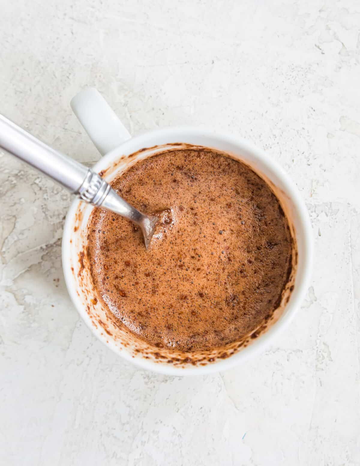 A mug filled with chocolate mug cake ingredients and a spoon in it.