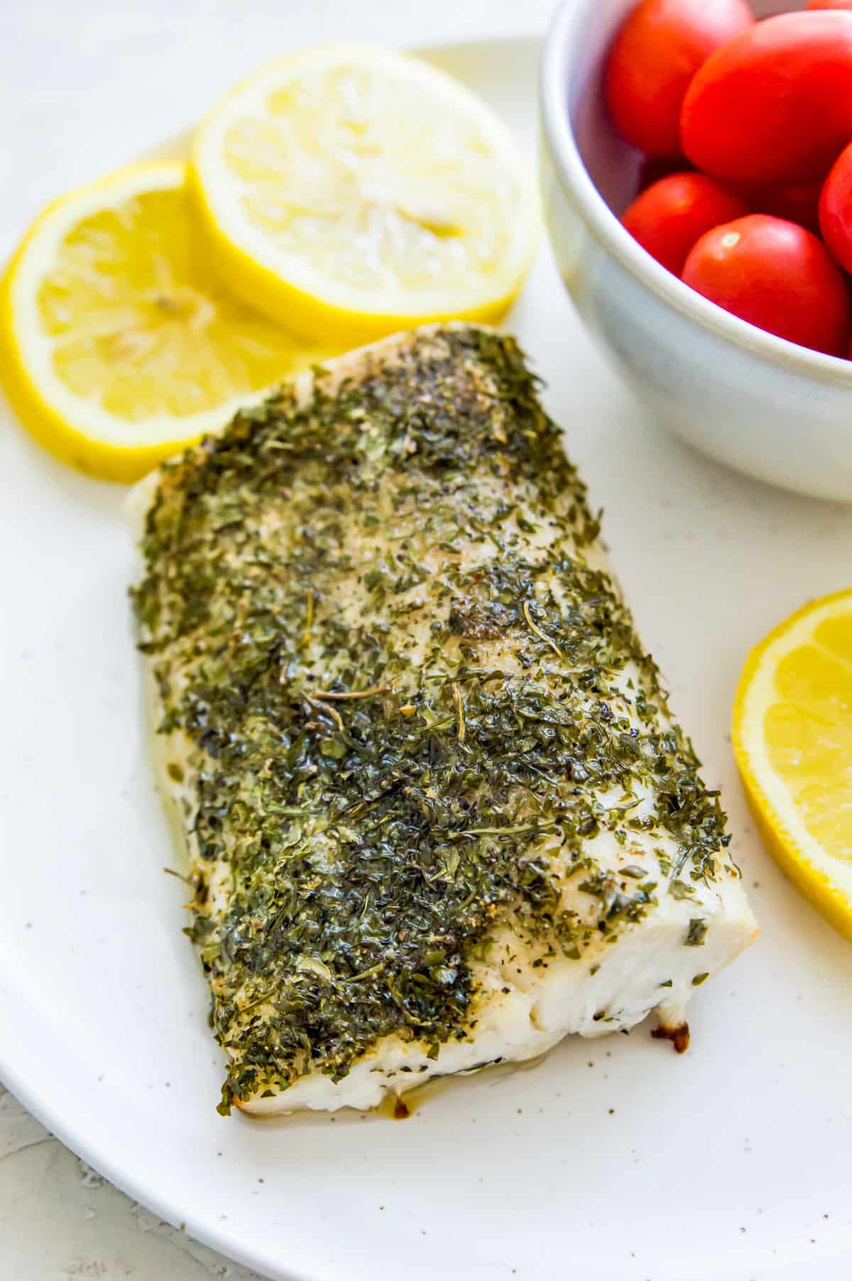 A piece of cooked Mahi Mahi on a plate with lemon slices beside it.