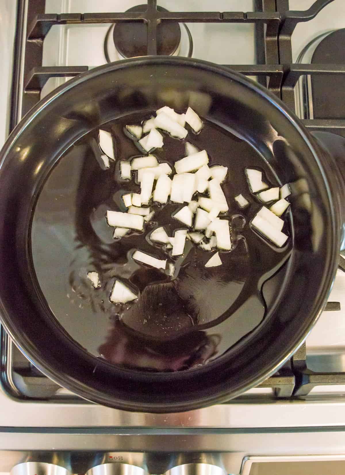 A pan filled with melted oil and chopped onions on the stovetop.