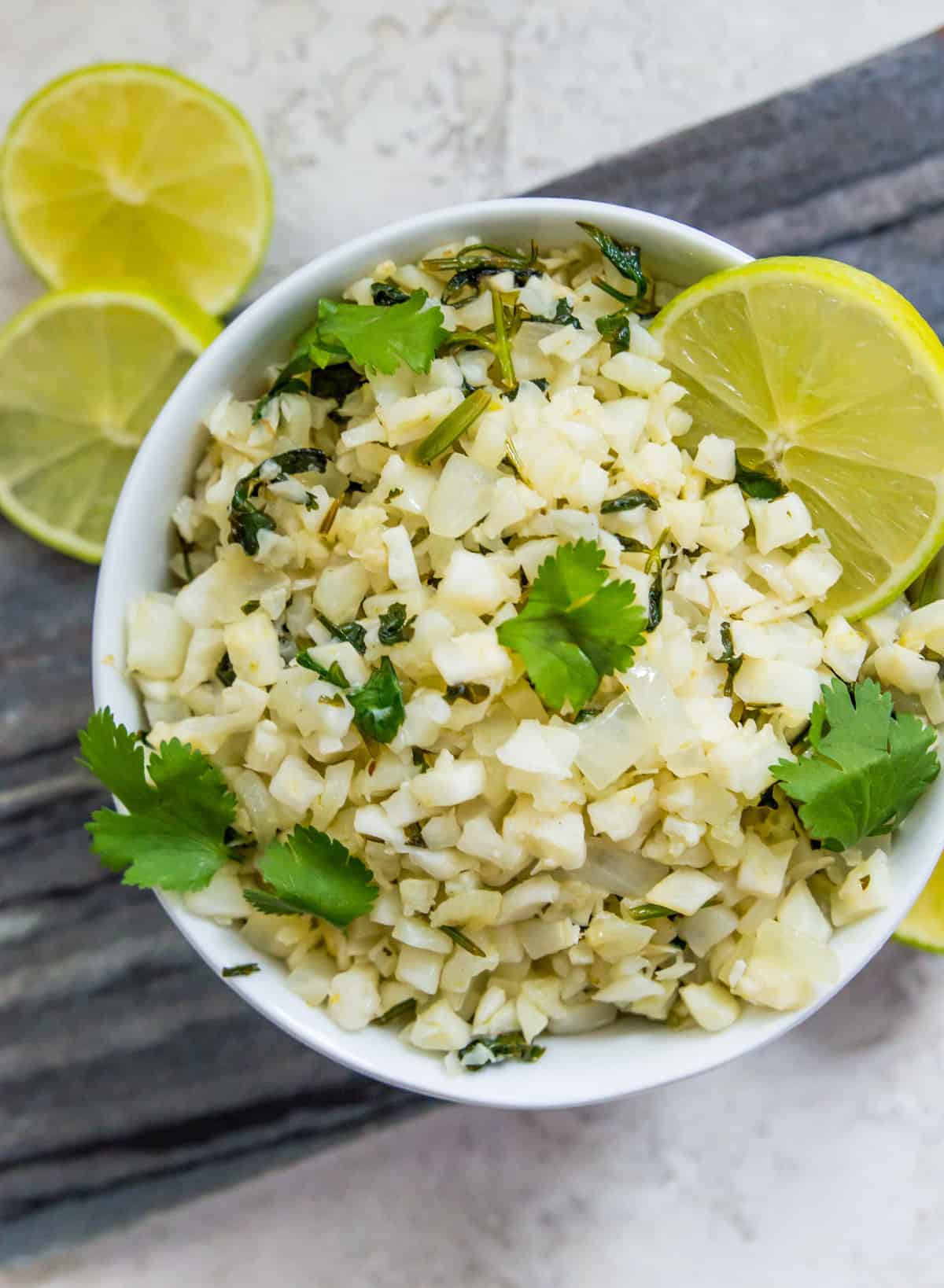 A bowl of cilantro lime cauliflower rice garnished with cilantro and with lime wedges in it.