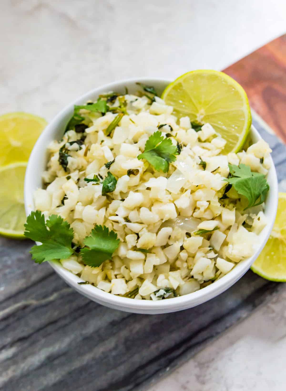 A bowl of cilantro and lime cauliflower fried rice garnished with fresh cilantro and lime wedges. 