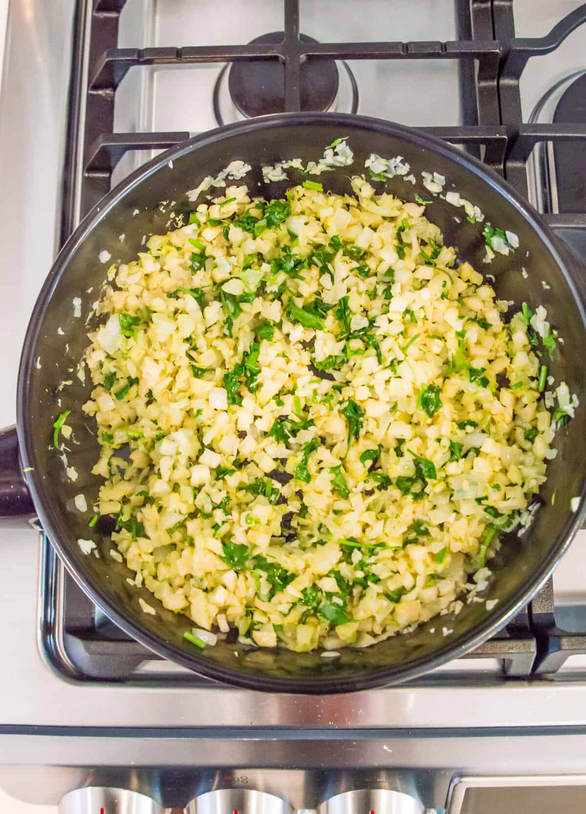 A pan full of cilantro lime cauliflower rice on the stovetop.