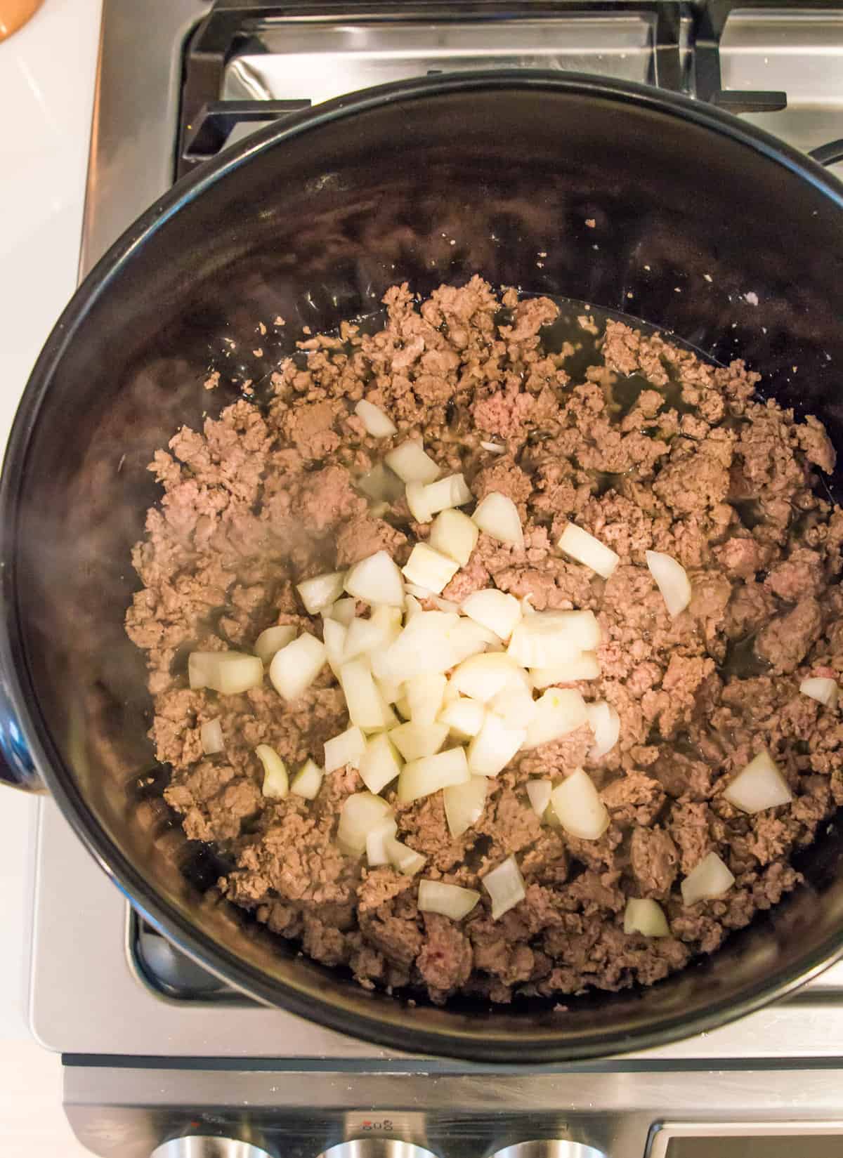 A pot on the stovetop with cooked ground pork and chopped white onion in it.