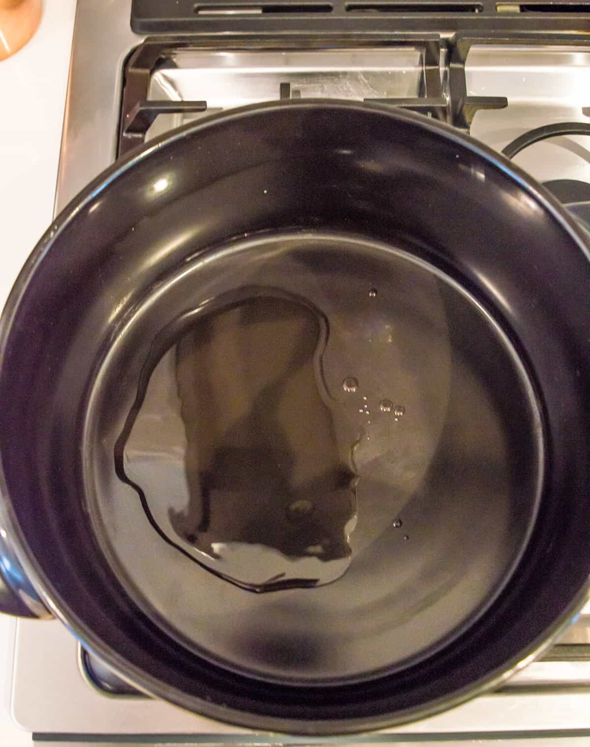 A large black ceramic pot on the stovetop with oil in it.