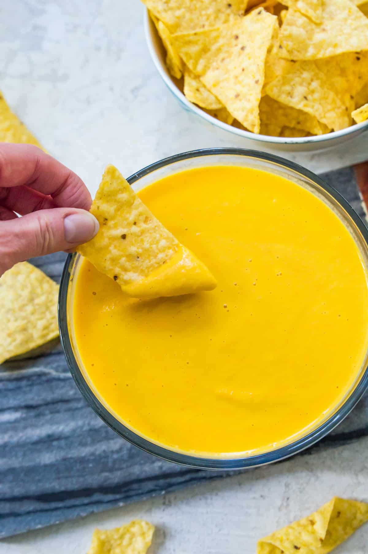 A bowl of vegan cheese sauce with a chip being dipped into it.