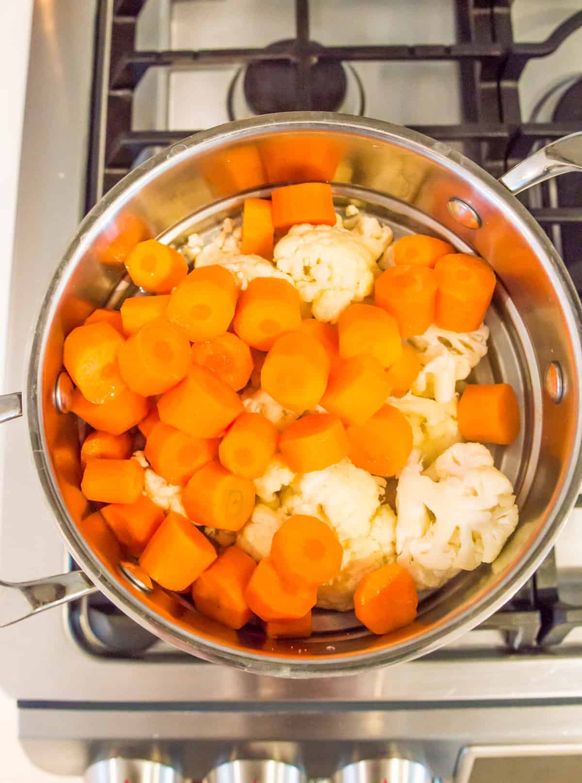 A pot on the stove with chopped carrots and cauliflower florets in it.