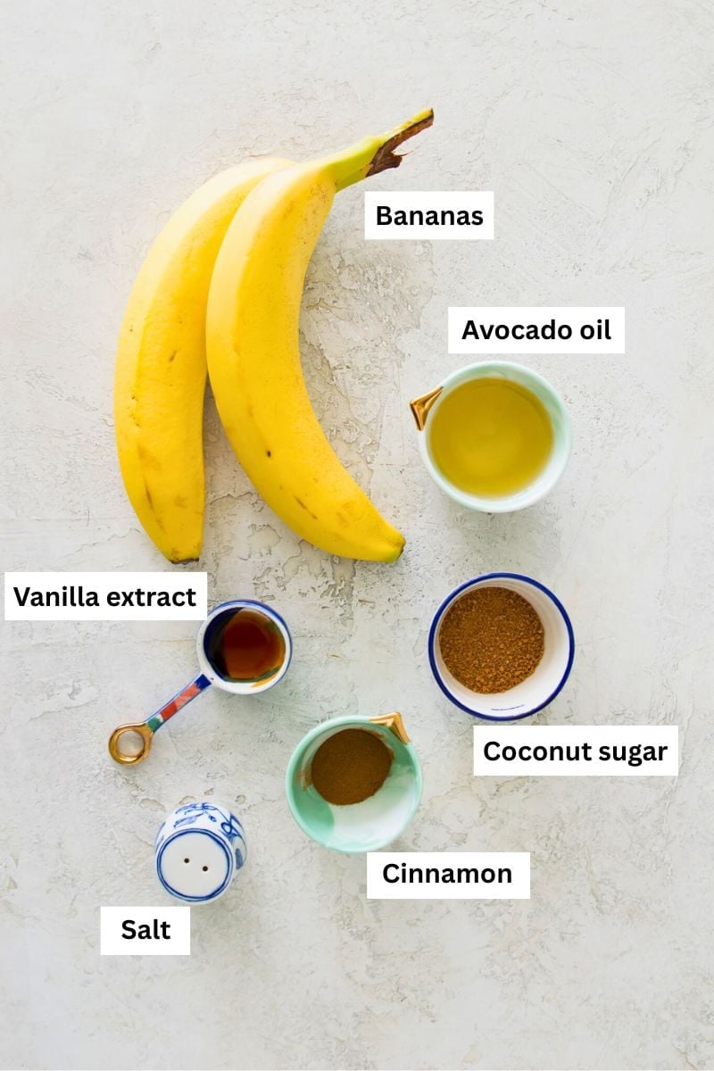 Two bananas and jars of avocado oil, coconut sugar, ground cinnamon and vanilla extract.