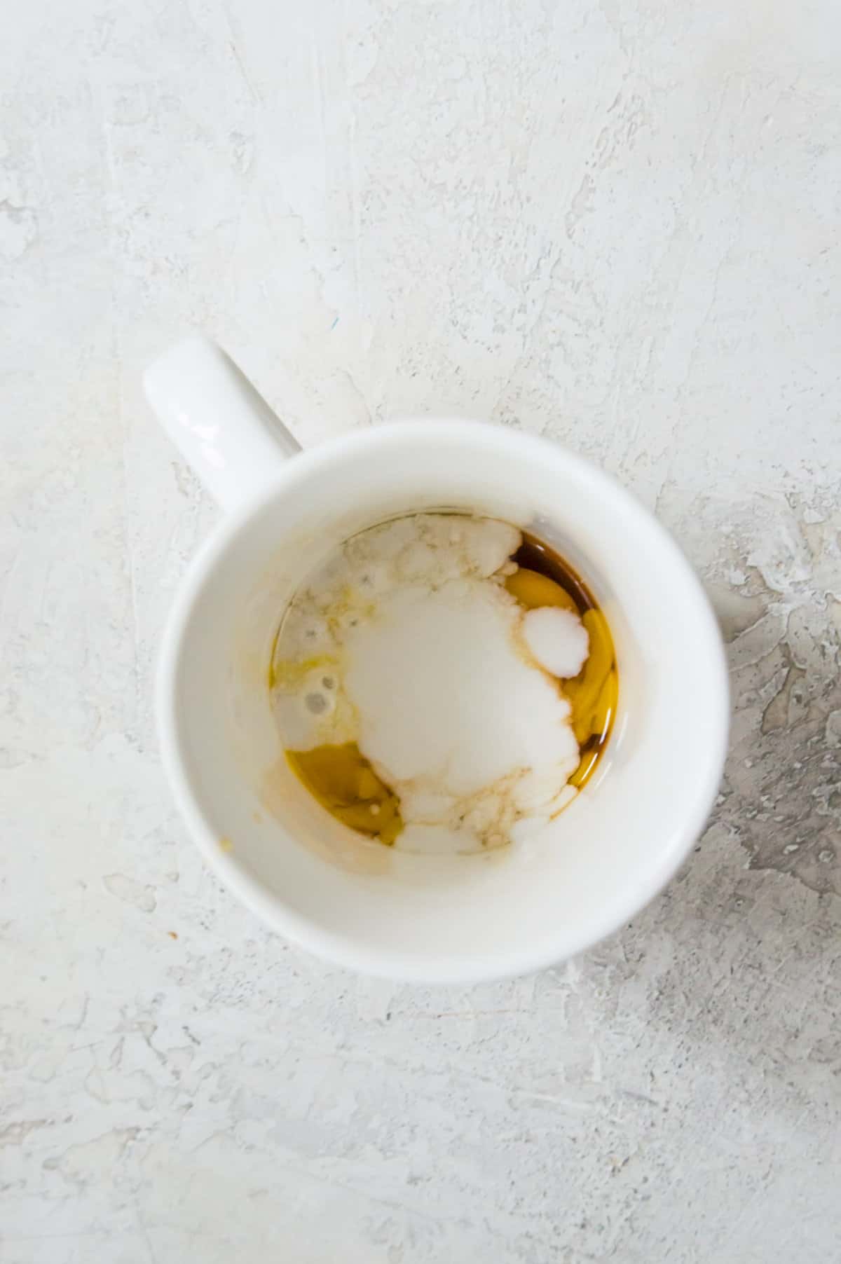 A mug with an egg, maple syrup and coconut milk in it.
