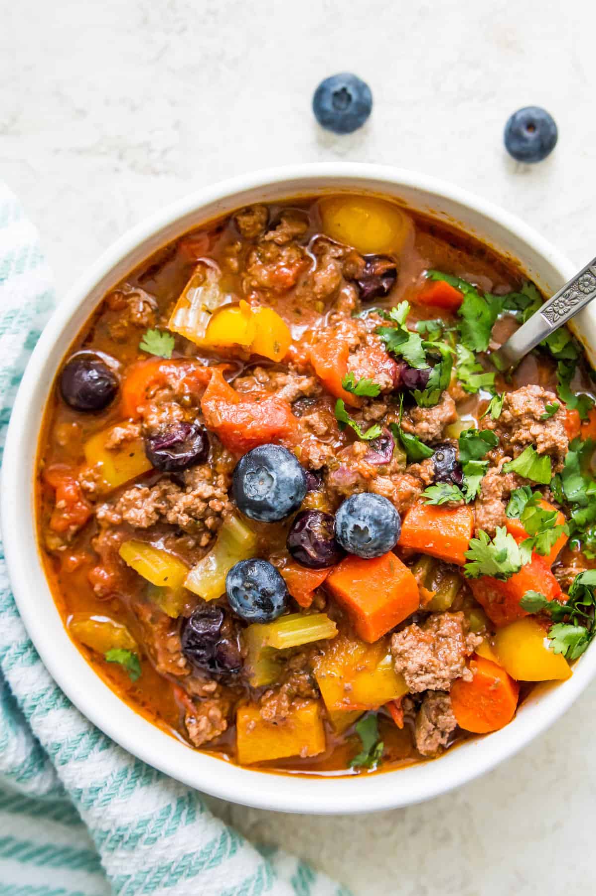 A bowl of no bean chili topped with fresh, chopped cilantro and blueberries.