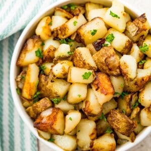 A bowl of southern fried potatoes and onions topped with fresh parsley.
