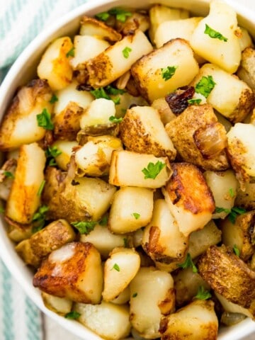 A bowl of southern fried potatoes and onions topped with fresh parsley.