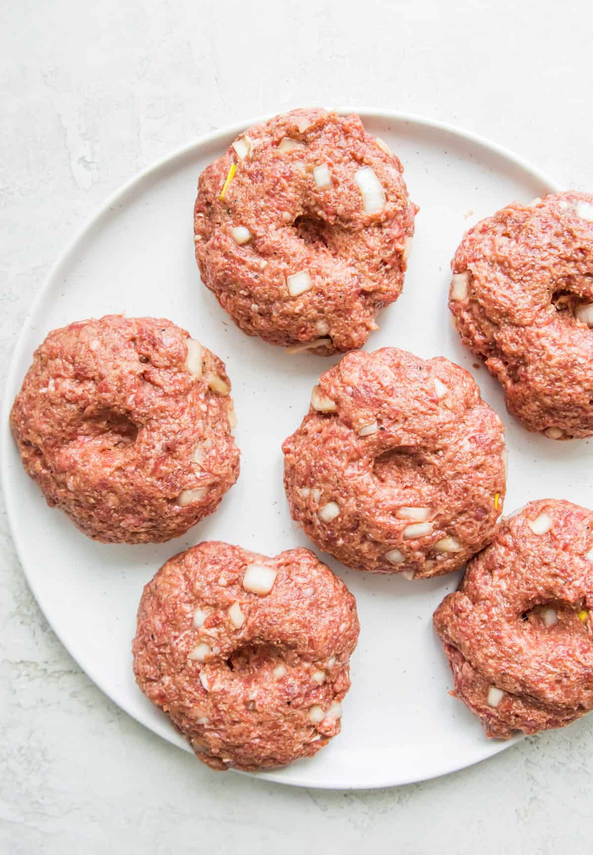 Six uncooked burger patties on a white place. 