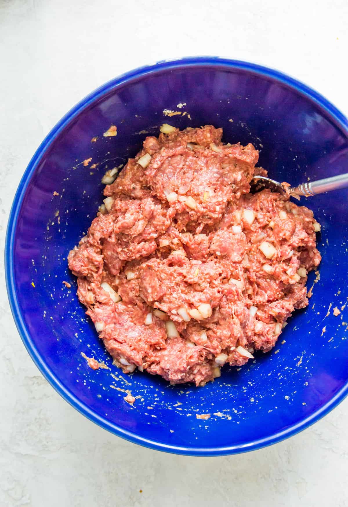 A ground beef meat mixture in a large blue bowl with a spoon in it. 