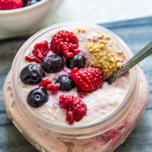 A jar of berry cheesecake overnight oats topped with fresh berries with a spoon in it.